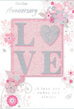 This anniversary card appears as a gentle celebration of long-lasting romance, its entire surface washed in soft pastel pinks and silvery greys that evoke the hush of an early evening walk through Wealdstone's quiet residential streets. At the centre, the word "LOVE" stands out in raised, softly sparkling glitter, its letters rounded and elegant, with the "O" transformed into a shimmering silver heart that feels both playful and deeply affectionate. The textured glitter gives the impression of delicate sugar crystals dusted over each curve, making the central motif both visually striking and deliciously tactile. Surrounding this focal word, clusters of delicate blooms in blush, mauve, and the palest ivory unfold with an almost watercolour softness, their edges slightly blurred, as though brushed gently with a wet paintbrush. Fine, flowing lines suggest stems and tendrils, weaving around the flowers in relaxed arcs like the natural drape of a hand-crafted bouquet. Tiny details-small petals, swirling flourishes, and discreet butterfly silhouettes-add a sense of movement and quiet whimsy, reminiscent of an English spring garden or the floral displays seen near local Wealdstone cafés. The background remains a calm blush tone, allowing the silver accents and floral details to stand out without overwhelming the eye. In graceful script, the words "On Our Anniversary" and "I love you today and always" appear in carefully placed lines, their typography elegant yet unpretentious, echoing the sincerity of a spoken promise. The overall design feels like a whispered vow translated into paper form, a tender keepsake that would pair beautifully with a soft, romantic arrangement delivered to a home in Wealdstone by a local florist who understands the language of flowers and lasting love.